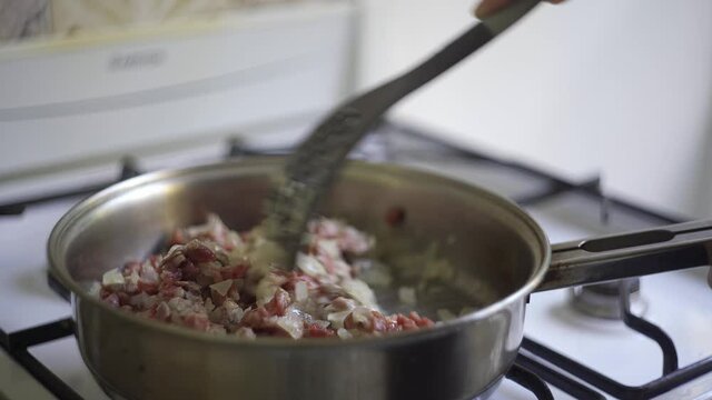 Mixing a meat and onion filling in a pan while is on the stove.