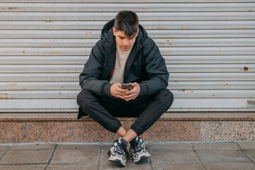 young man sitting on the street with mobile phone