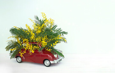 Red Toy Car With Bouquet Of Bright Mimosa Flowers. Image with Soft Focus And Bokeh