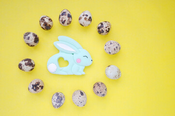 Festive photo with Easter bunny and quail eggs. Top view on a yellow background. Easter. Copyspace.