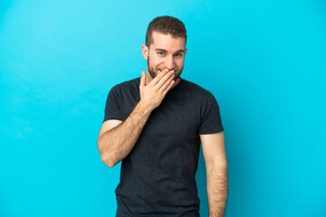 Young handsome caucasian man isolated on blue background happy and smiling covering mouth with hand