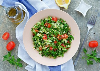 Tabbouleh, parsley, tomato and cucumber vegetable salad with bulgur in a clay plate on a gray concrete background. Salad recipes. Healthly food.