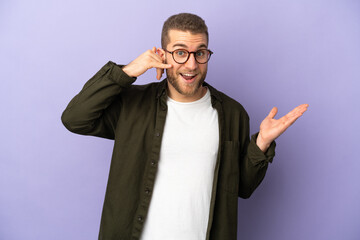 Young handsome caucasian man isolated on purple background making phone gesture and doubting