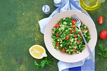 Tabbouleh, parsley, tomato and cucumber vegetable salad with bulgur in a clay plate on an olive concrete background. Salad recipes. Healthly food.