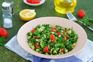 Tabbouleh, parsley, tomato and cucumber vegetable salad with bulgur in a clay plate on an olive concrete background. Salad recipes. Healthly food.