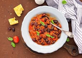 Large beans stewed with tomatoes, apple and bell peppers in a gray plate on a brown concrete background. Vegetarian and vegan food. Healthy eating.