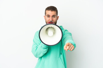 Young handsome caucasian man isolated on white background shouting through a megaphone to announce something while pointing to the front
