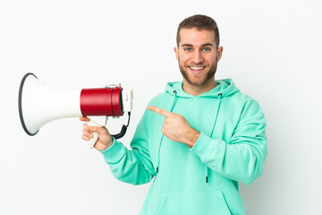 Young handsome caucasian man isolated on white background holding a megaphone and pointing side