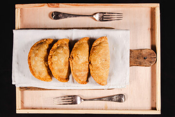 zenithal photograph of four empanadas with two forks on a wooden table.