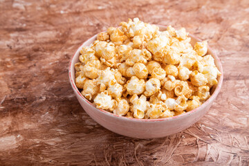 Popcorn with caramel in ceramic bowl on brown concrete background. Side view.