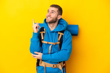 Young caucasian mountaineer man with a big backpack isolated on yellow background pointing up a great idea