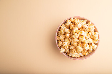Popcorn with caramel in ceramic bowl on pastel orange background. Top view, copy space.