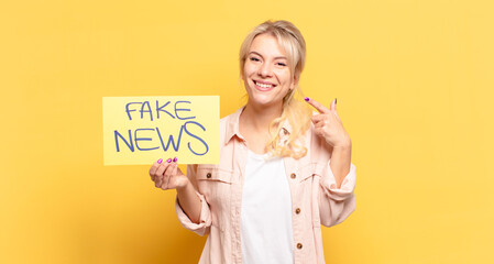 blonde woman smiling confidently pointing to own broad smile, positive, relaxed, satisfied attitude