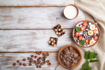 Chocolate cornflakes with milk and strawberry in wooden bowl on white wooden background. Top view, copy space.
