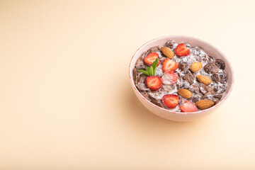 Chocolate cornflakes with milk, strawberry and almonds in ceramic bowl on pastel orange background. Side view, copy space.