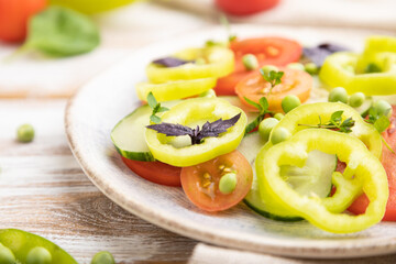 Vegetarian salad from green pea, tomatoes, pepper and basil on white wooden background. Side view, selective focus.