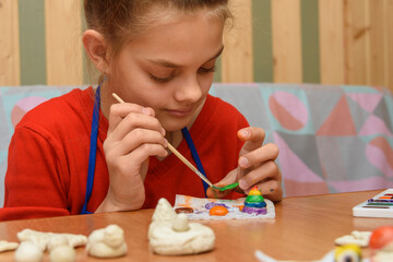 A girl at home paints a craft made from salt dough