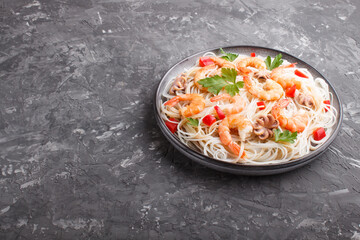 Rice noodles with shrimps or prawns and small octopuses on gray ceramic plate on a black concrete background. Side view.