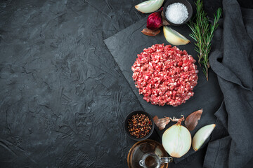 Fototapeta na wymiar Fresh, juicy minced meat with rosemary, onion, pepper and salt on a black background. Top view, horizontal. Cooking concept.