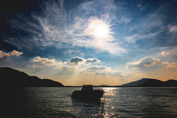Silhouette of a boat standing on the water. Backlit with cloudy sky