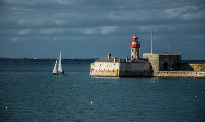 Un velero de recreo sale del puerto de Dún Laoghaire con un faro rojo al fondo.