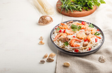 Rice noodles with shrimps or prawns and small octopuses on gray ceramic plate on a white wooden background. side view, copy space.