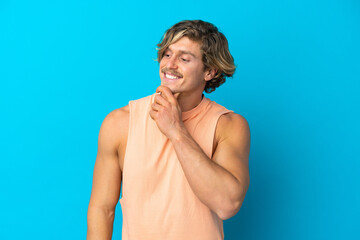 Handsome blonde man isolated on blue background looking to the side and smiling