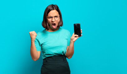 young hispanic woman shouting aggressively with an angry expression or with fists clenched...
