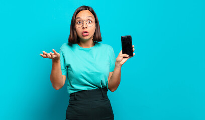 young hispanic woman feeling extremely shocked and surprised, anxious and panicking, with a...