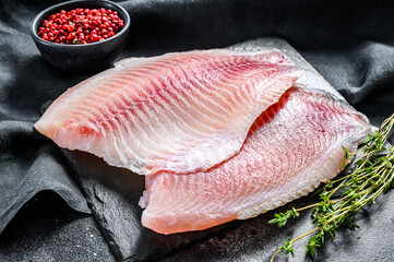 Fresh tilapia fillet on a chopping Board with thyme. Black background. Top view