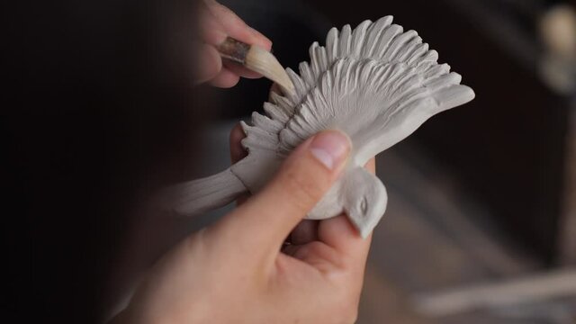 Close up portrait of potter woman hands working on details of a clay handcraft bird. Work with different pottery tools. Concept of creative ceramics. Start up business, artwork and interior