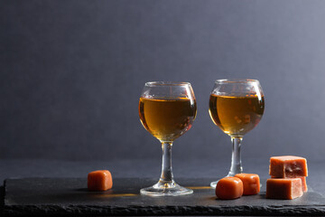 Glass of whiskey with caramel candies on a black stone slate board on black background. Side view,...