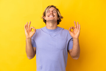 Handsome blonde man isolated on yellow background in zen pose