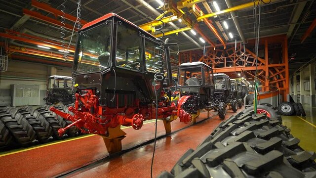 The tractor cab is suspended in the workshop on a crane beam, the engine is at the bottom. Assembly of tractor tractors, camera movement.