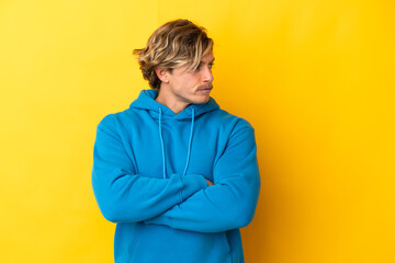 Handsome blonde man isolated on yellow background keeping the arms crossed