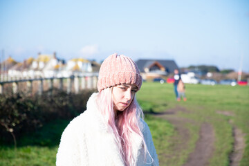 Young woman or girl with pink hair and pink hat wearing a white coat in winter.