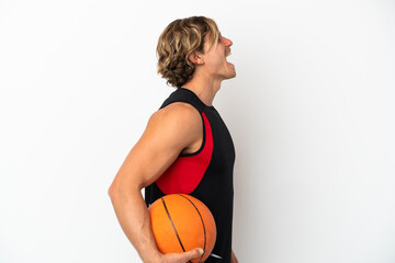 Young blonde man holding a ball of basketball isolated on white background laughing in lateral position
