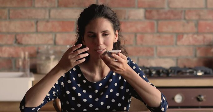 Woman sit in kitchen hold smartphone make call talk to friend use speakerphone, share voicemail, presses microphone button record leave audio message, artificial intelligence modern tech usage concept