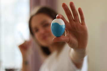 Young Woman holds Easter Egg in outstretched hand. Painting Easter Eggs at home concept. 