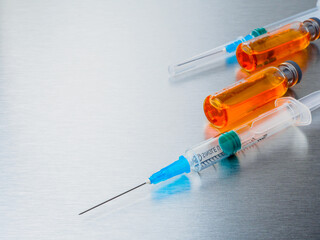 Selective focus. Close-up shot of injection syringes and ampoules with orange coronavirus vaccine on a silver aluminum background. Covid-19 pandemic medical concept. Copy space.