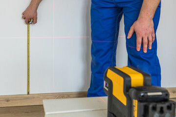 A specialist makes measurements on the wall with a measuring stick and an electronic laser to...