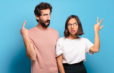 young couple feeling confused and puzzled, showing you are insane, crazy or out of your mind