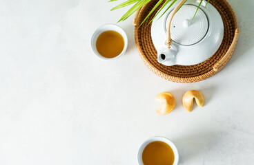 Asian tea concept mockup, two white cups of tea and teapot surrounded with green tea dry leaves view from above, space for a text on white background - obrazy, fototapety, plakaty
