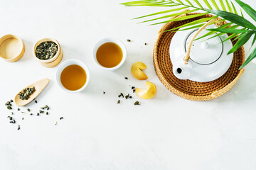 View from above of Asian tea concept, two white cups of tea, fortune cookies and teapot surrounded with dry green tea on light background. - obrazy, fototapety, plakaty