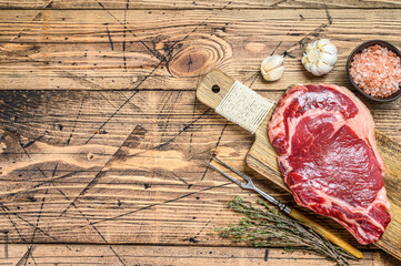 Raw rib eye steak on the bone. Marble beef meat ribeye. wooden background. Top view. Copy space