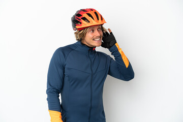 Young blonde cyclist man isolated on white background listening to something by putting hand on the ear