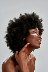 Beauty portrait of attractive young naked african american woman with afro hair applying cream on...