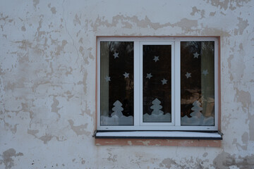 old concrete building facade with a white plastic window showing Christmas decorations that the ceiling is made of paper