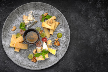 Cheese plate, assorted cheeses with mint, candied fruit, honey and cookies, on a  plate, on a dark background