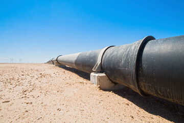 black tubes of a pipeline and power poles in the desert